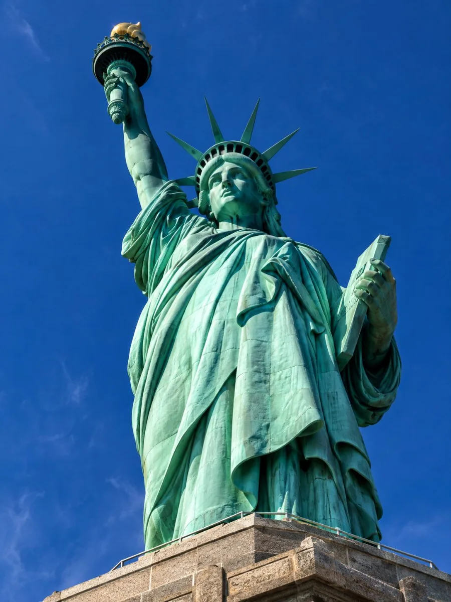 Looking up at the Statue of Liberty from the pedestal balcony, the green copper folds of the robe filling the frame against the sky