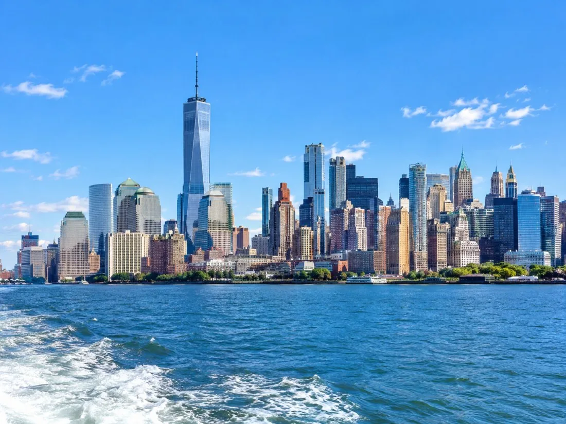 The Lower Manhattan skyline rising above blue harbor water, seen from a boat deck